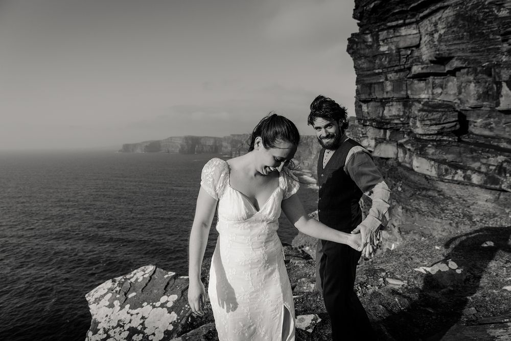 Couple laughing, holding hands at the edge of Cliffs of Moher during their adventure elopement in Ireland