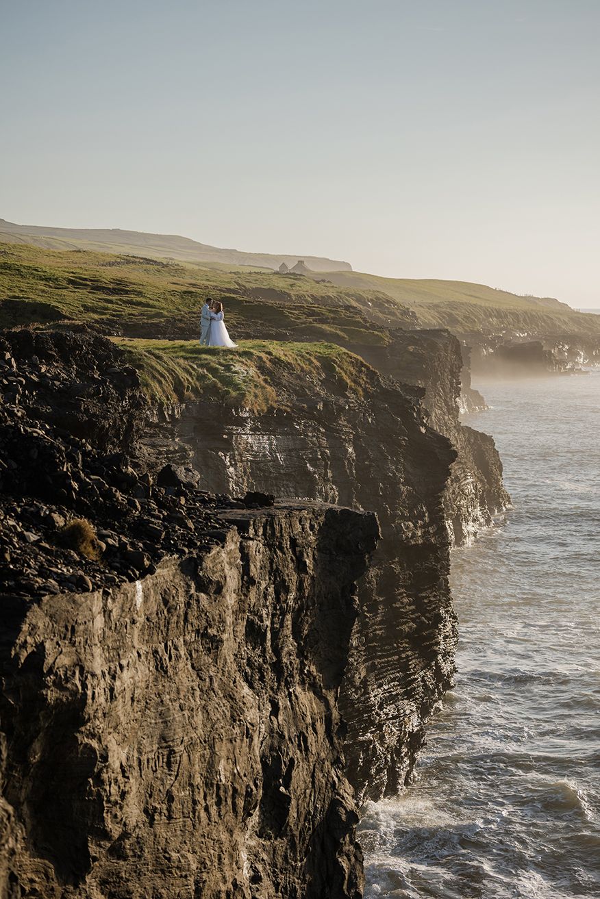 Couple standing, holding each other close, at the edge of Cliffs of Moher during their adventure elopement in Ireland