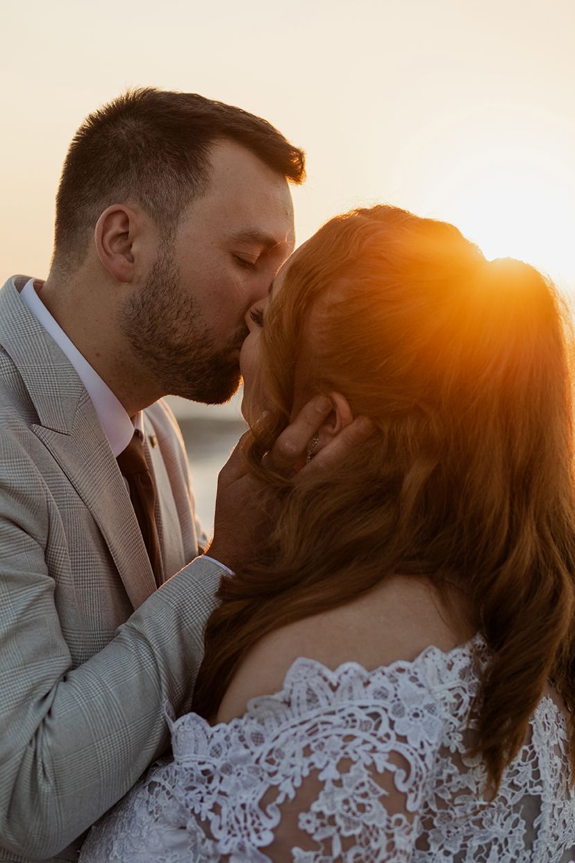 Elopement at Fanore beach, husband is kissing his wife as the sun sets at the horizon