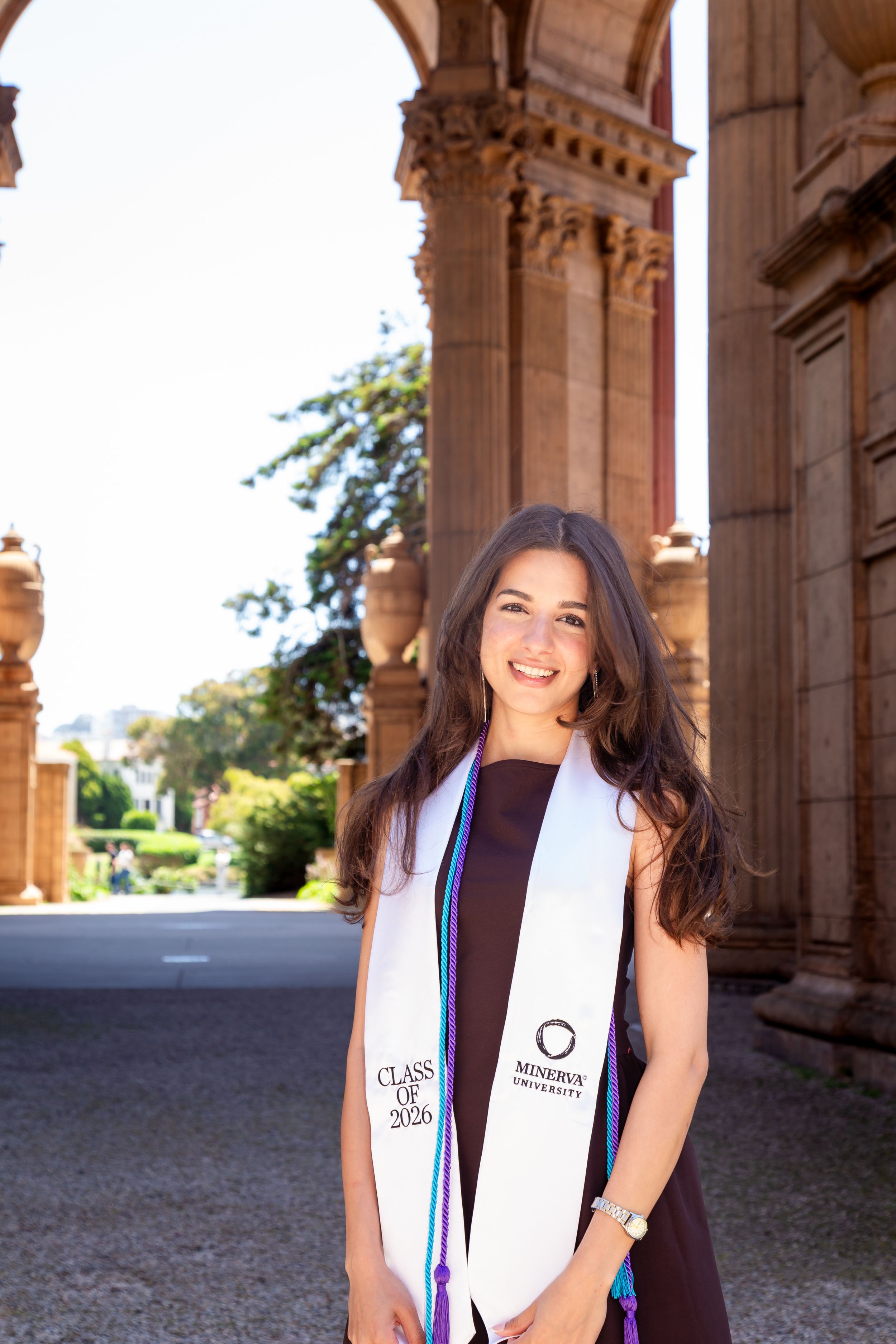 Smiling graduate wearing Minerva University Class of 2025 stole poses before ornate stone columns at Palace of Fine Arts.