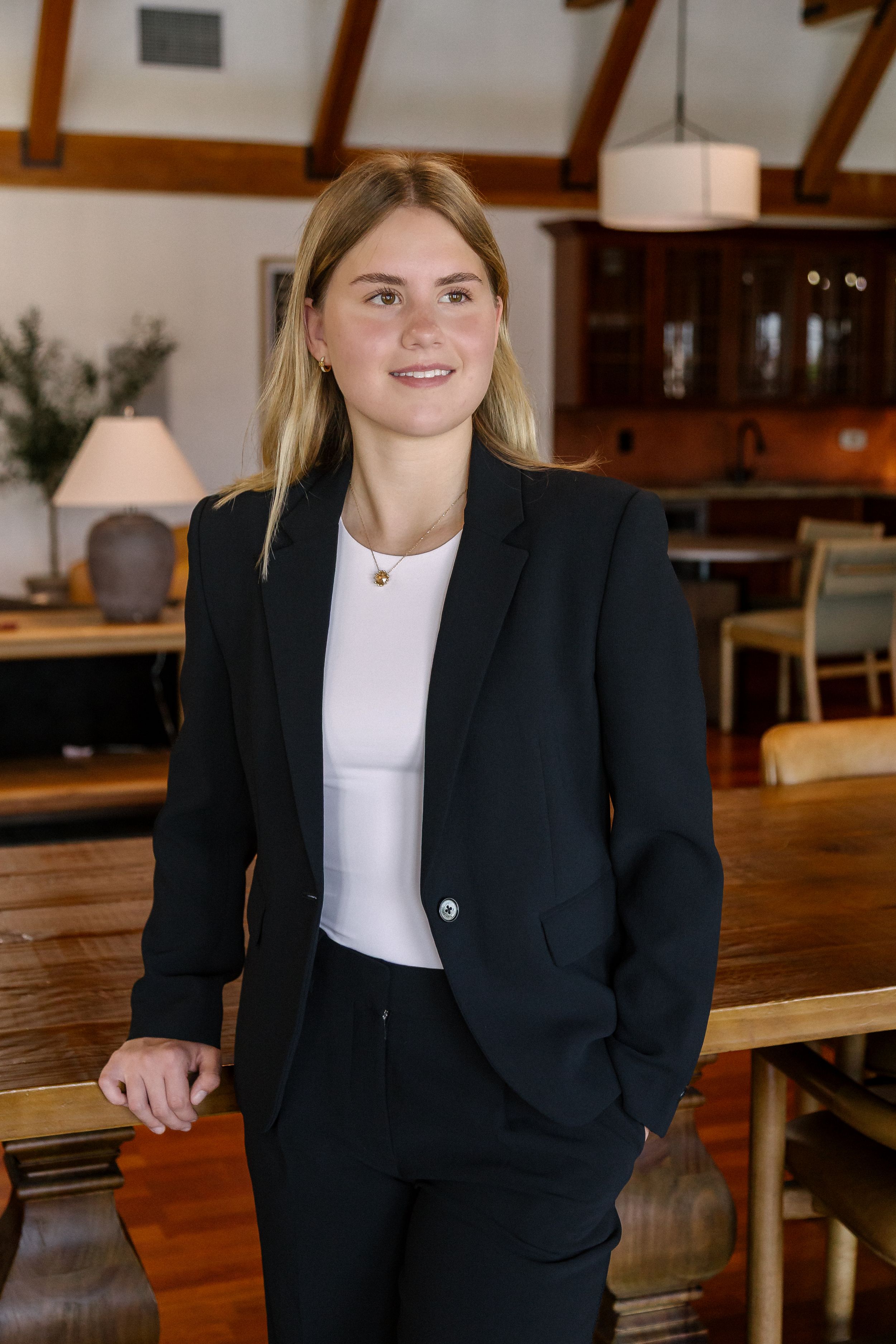 Young professional woman in black blazer and white top smiling in elegant restaurant setting.