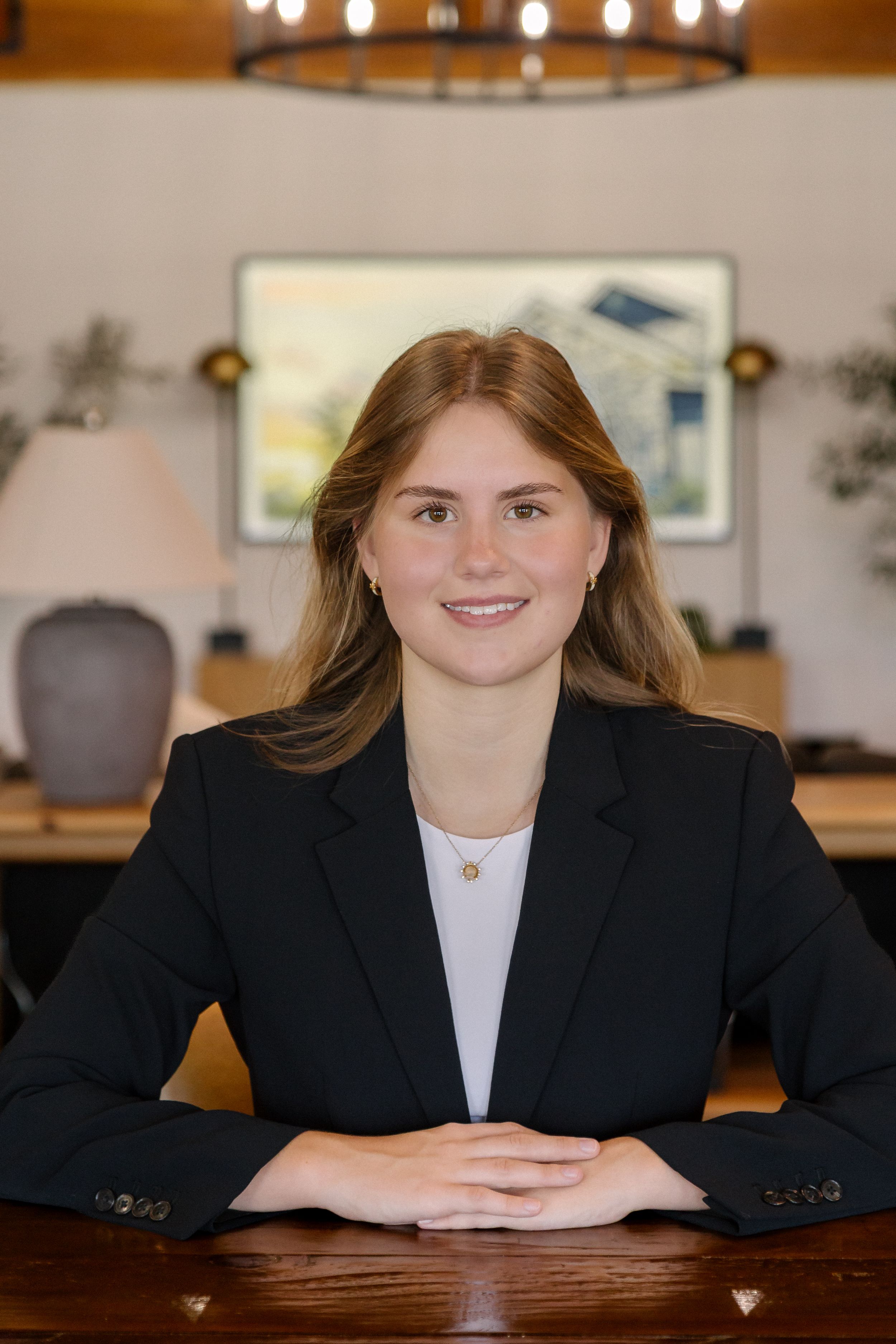 Young professional woman in black blazer smiling at desk in elegant office setting.