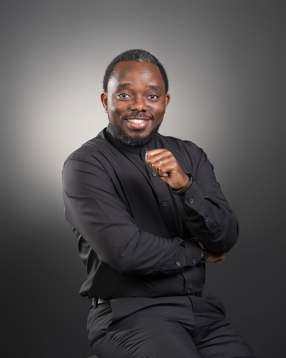 Smiling man in black shirt with arms crossed, professional studio portrait on gray background.