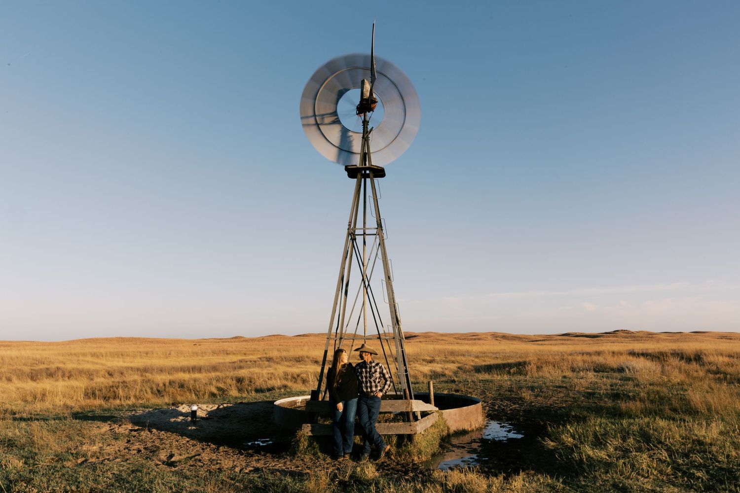 An old windmill spins against a bright blue sky on a sunny day.