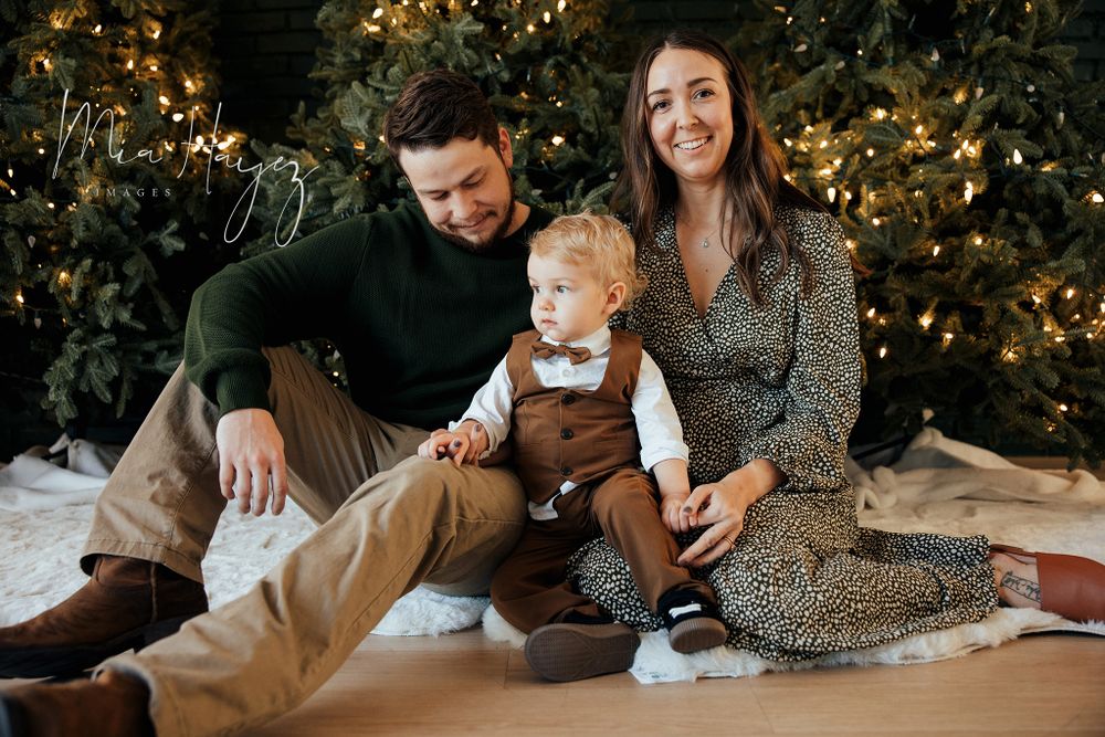 Family lying together on floor with Christmas tree and lights in background.