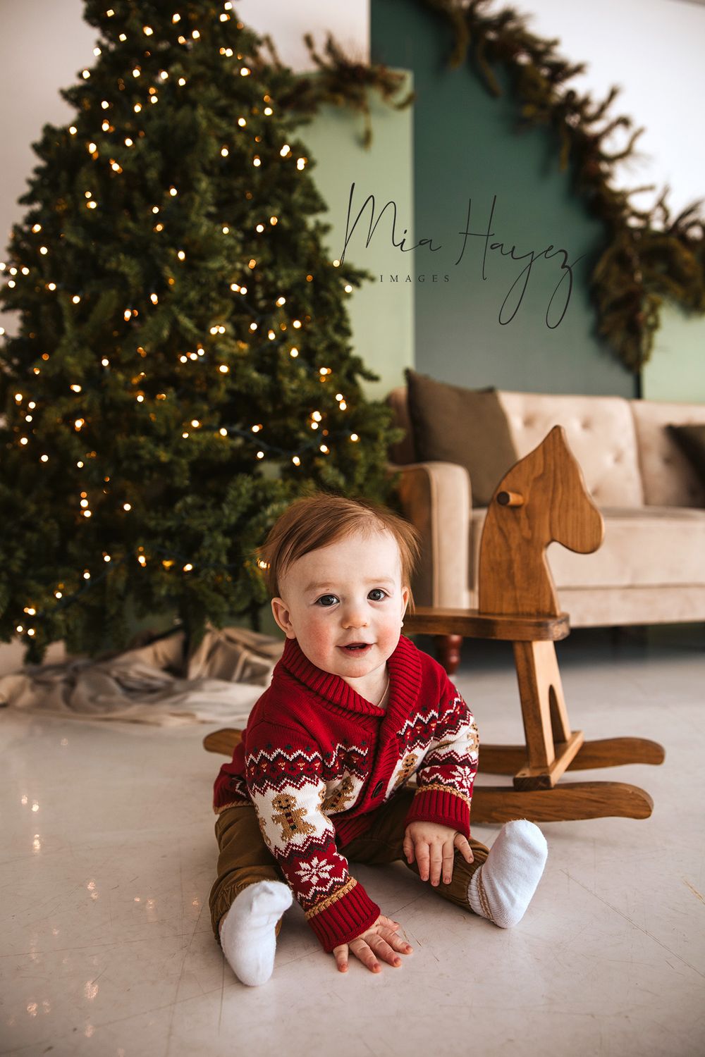 Holiday portraits featuring a baby in red sweater next to wooden rocking horse and Christmas tree.