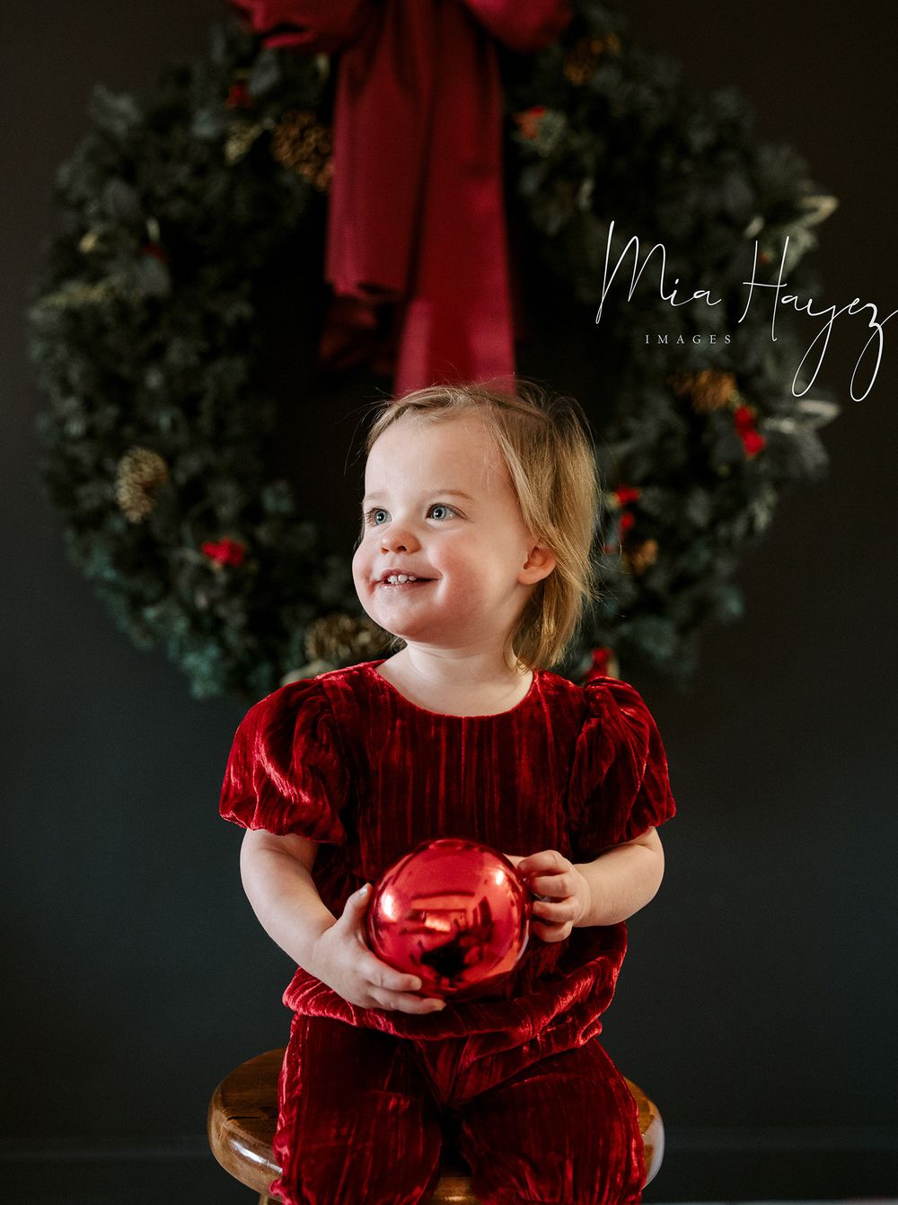 Baby wearing red velvet dress poses for holiday portraits with Christmas decorations.