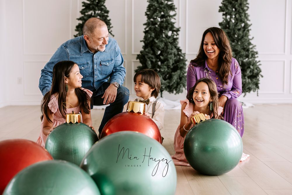 Family plays together with colorful exercise balls in front of Christmas trees.
