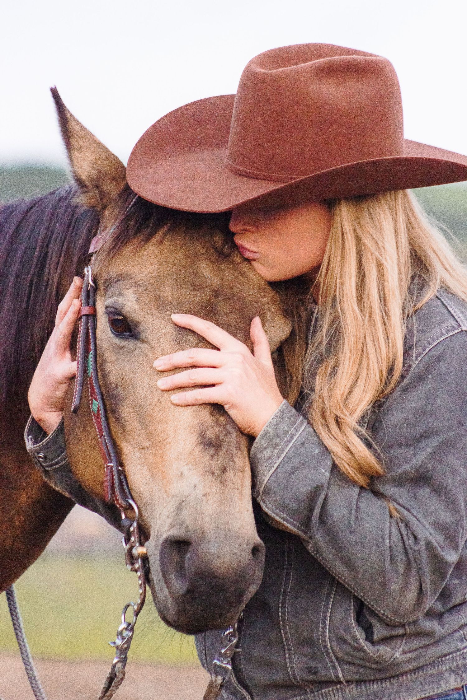 A western dressed woman holds her horse's head in her hands and hisses it's forehead.