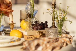 Close-up of a rustic table setting with fresh lemons, grapes, wildflowers and vintage glassware in warm sunlight.