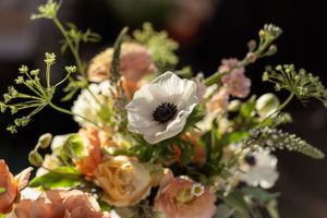 A romantic floral arrangement with white anemones, peach roses, and delicate green foliage in soft lighting.