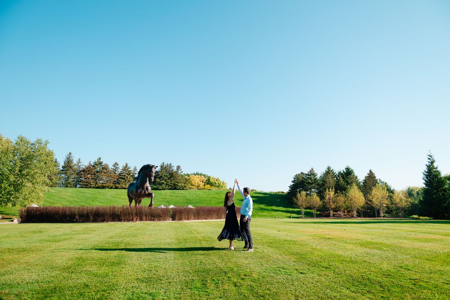 Golfers walk across a scenic green fairway on a sunny autumn day with trees lining the course.