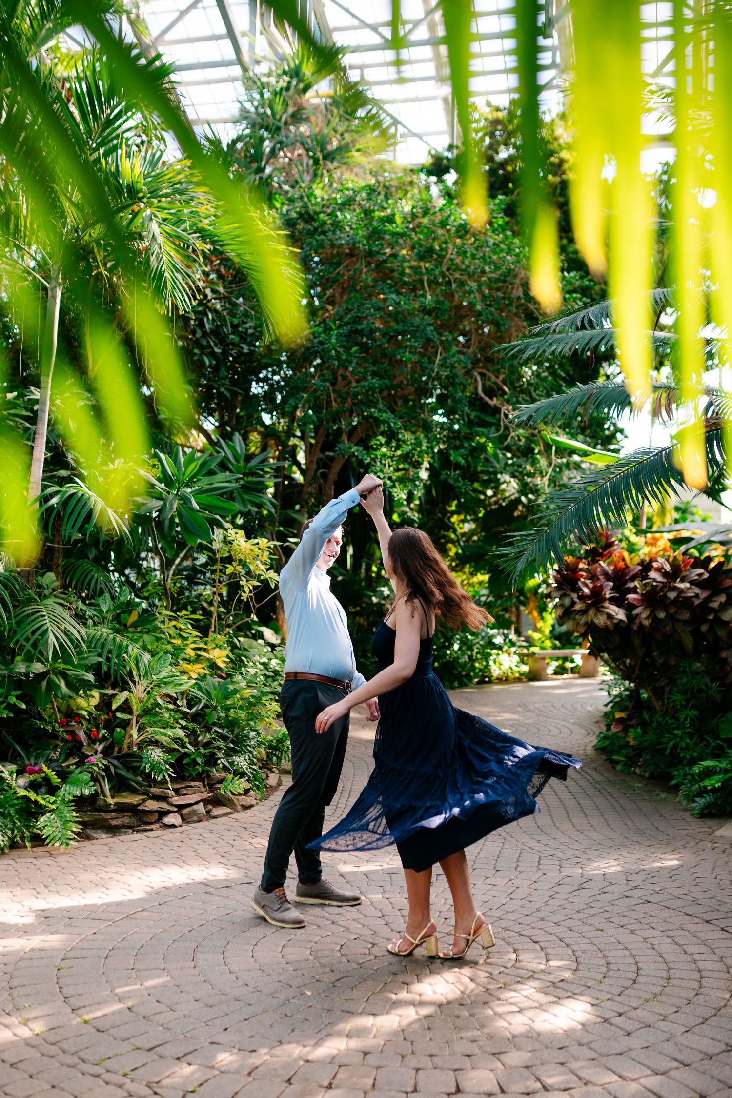 A sequence of dance moves captured on a curved brick pathway surrounded by lush tropical plants and palm fronds.