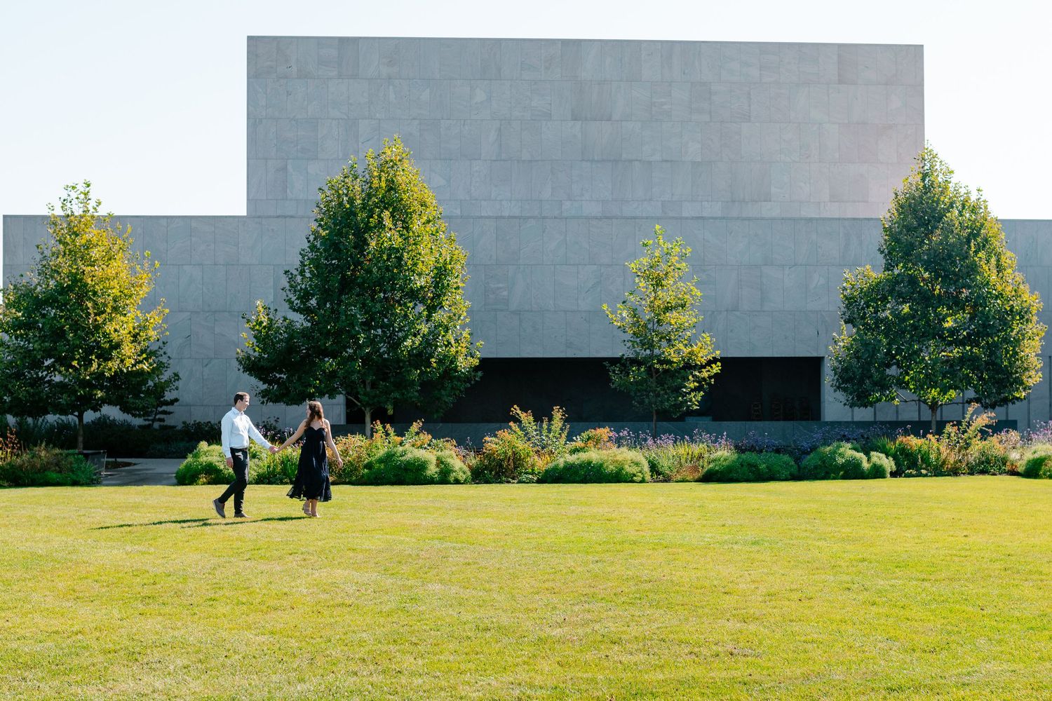 People walking across a grassy lawn in front of a modern building on a sunny day.