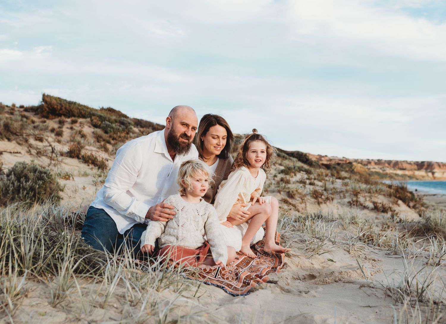 Coastal family photoshoot on rocky beach terrain under blue skies.