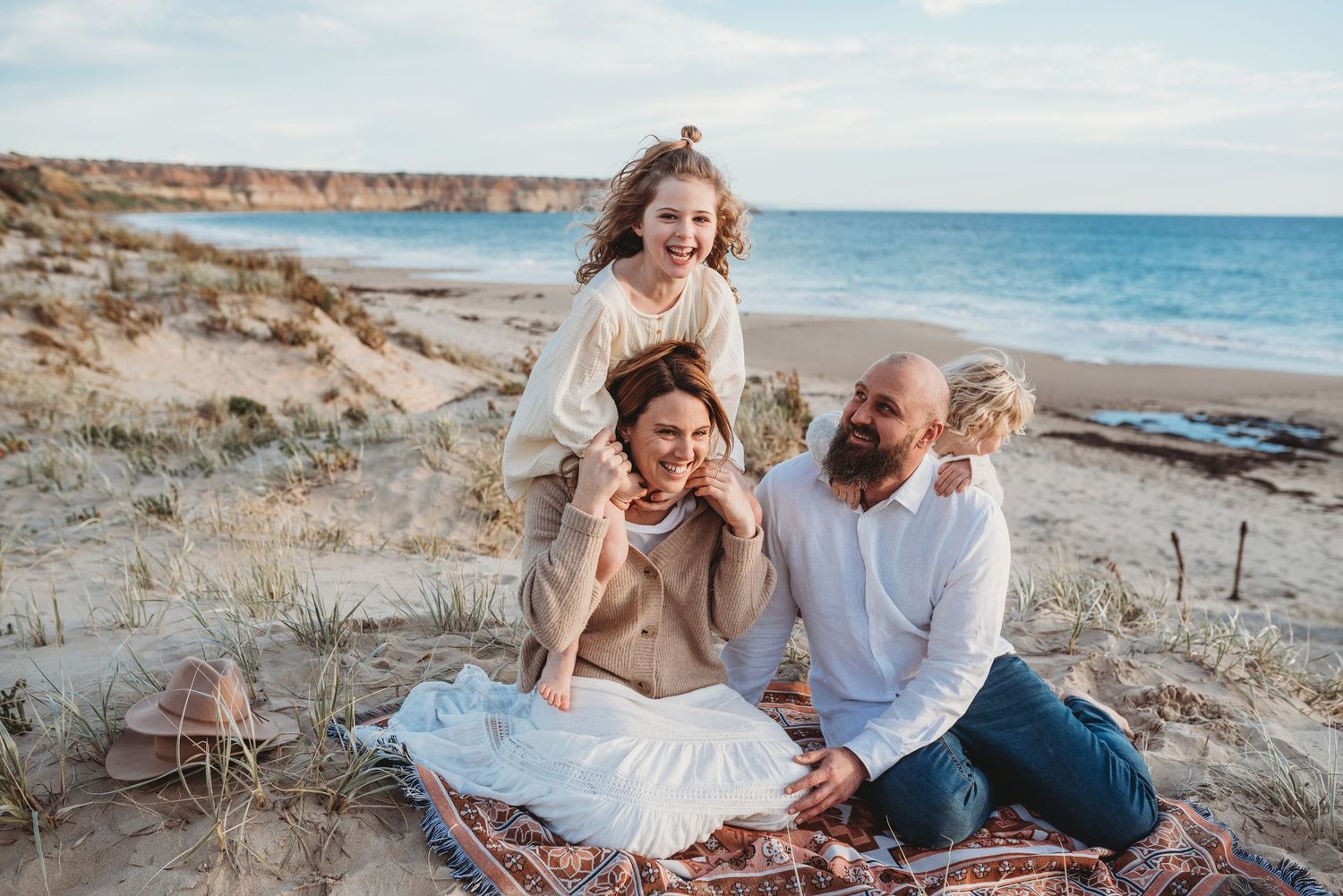 Family enjoying a playful moment together on a scenic beach with coastal cliffs in the background.