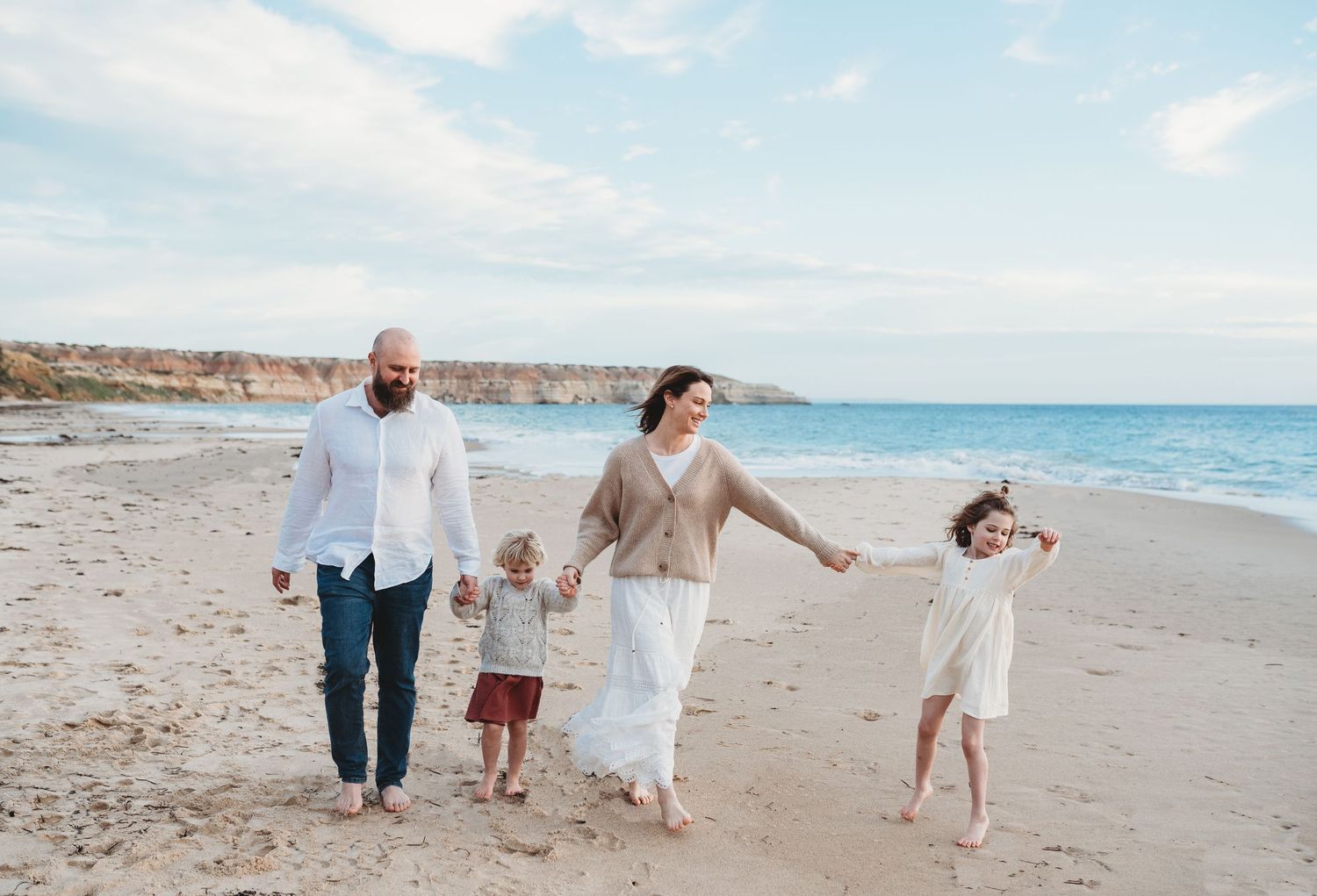 Family playing and running together on a sunny beach with coastal cliffs visible.