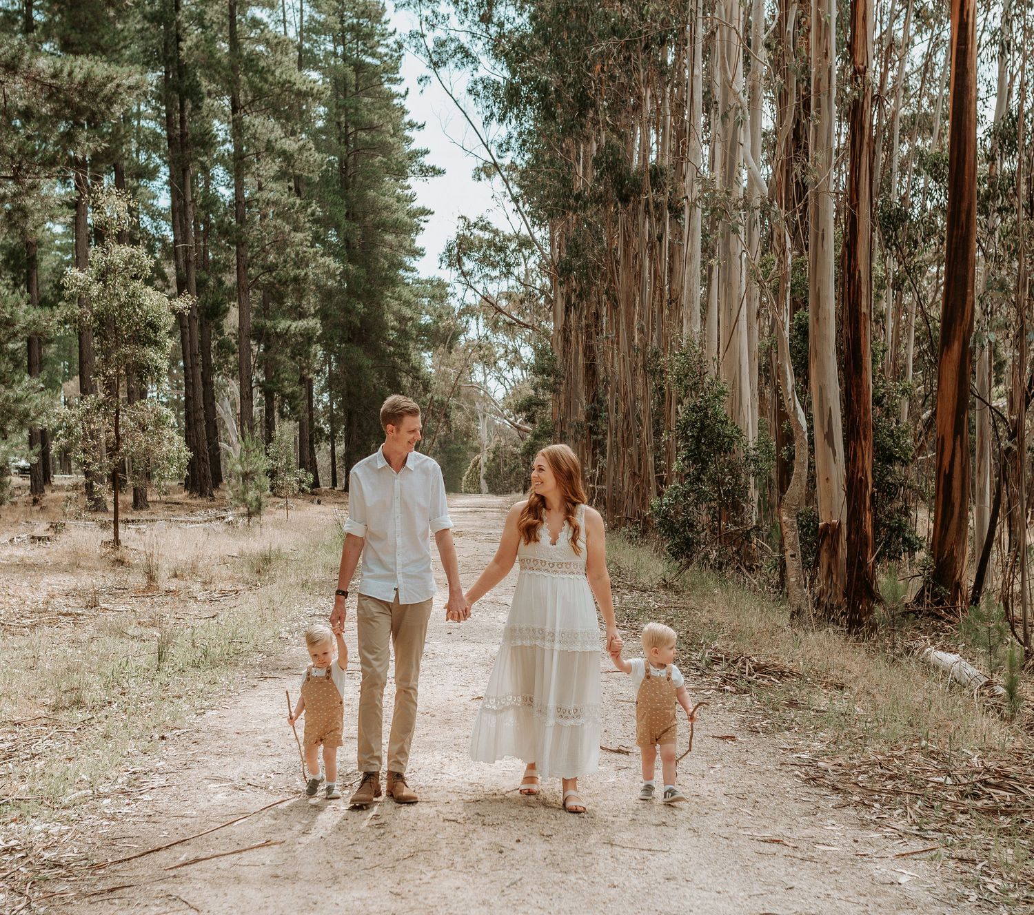 A family walks hand in hand down a forest path lined with tall eucalyptus trees.