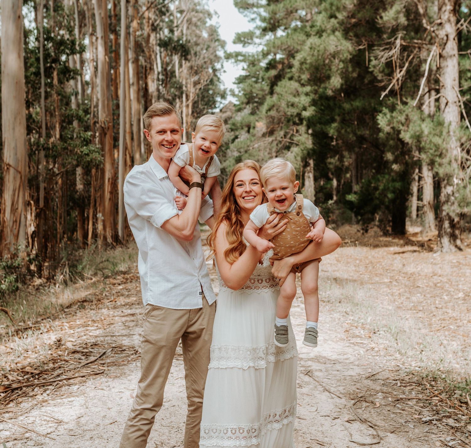 A couple shares joyful moments together on a tree-lined dirt path during a sunny outdoor photo session.
