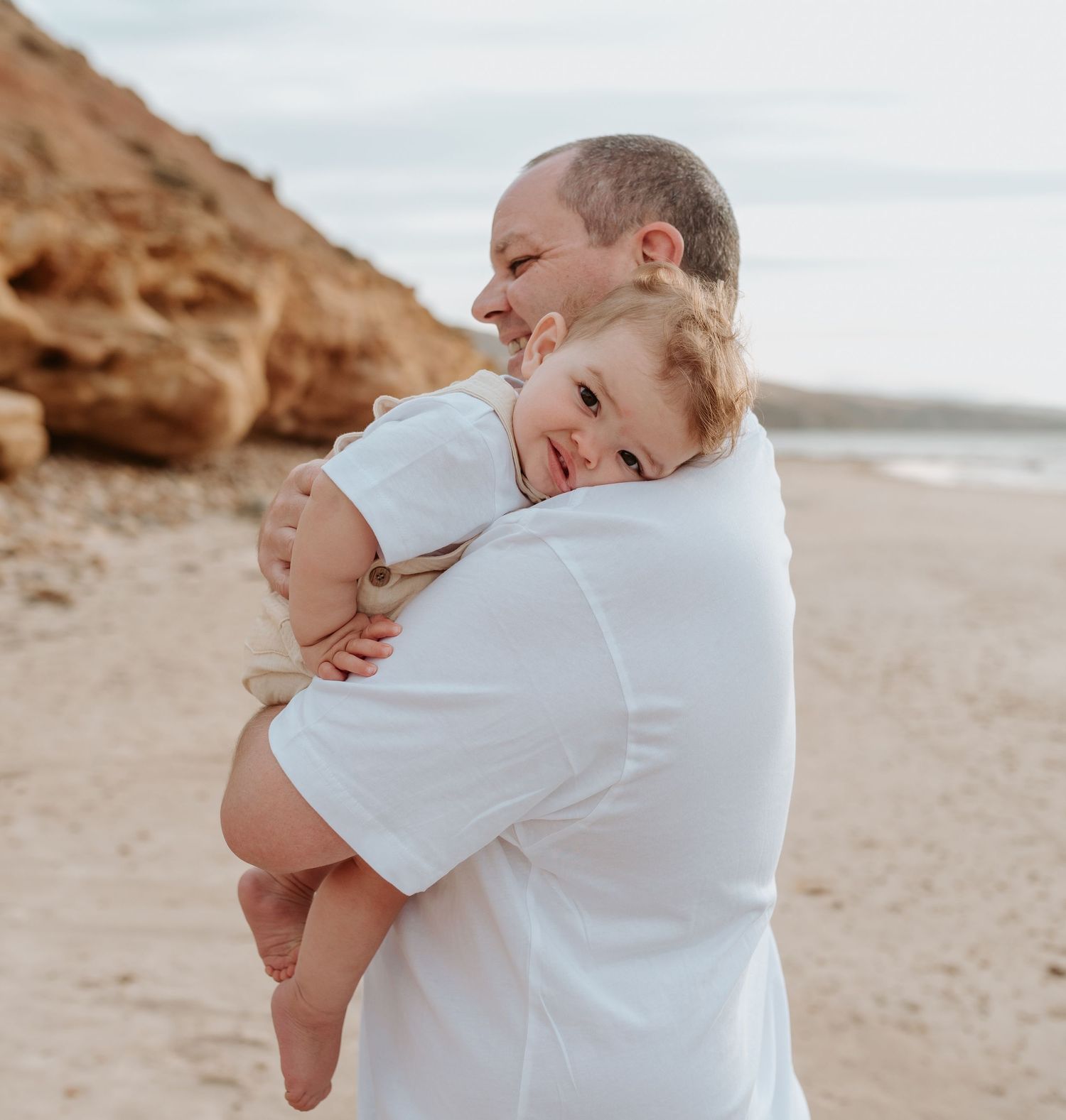 A joyful family moment captured at sunset on a beach with rocky cliffs in the background.