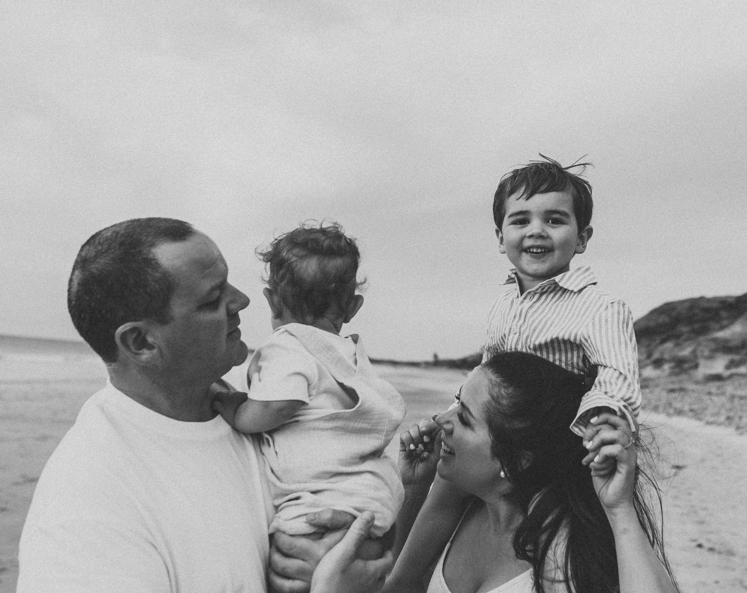 Candid black and white photos of a family playing and laughing together on the beach.