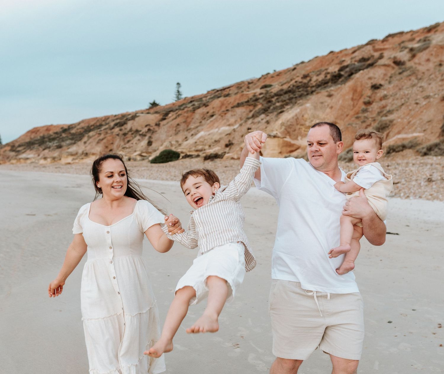 A family dressed in white having fun and playing together on a scenic beach with cliffs.