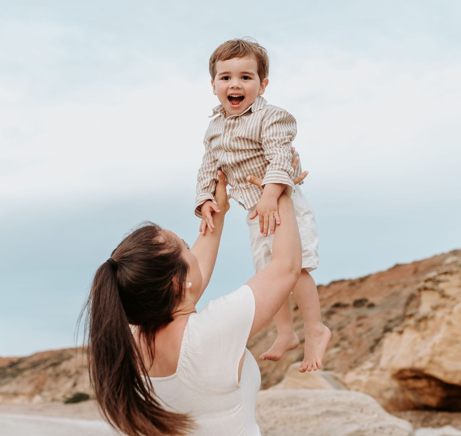 Candid shots of parents playing with their child on a sunny beach near rocky cliffs.