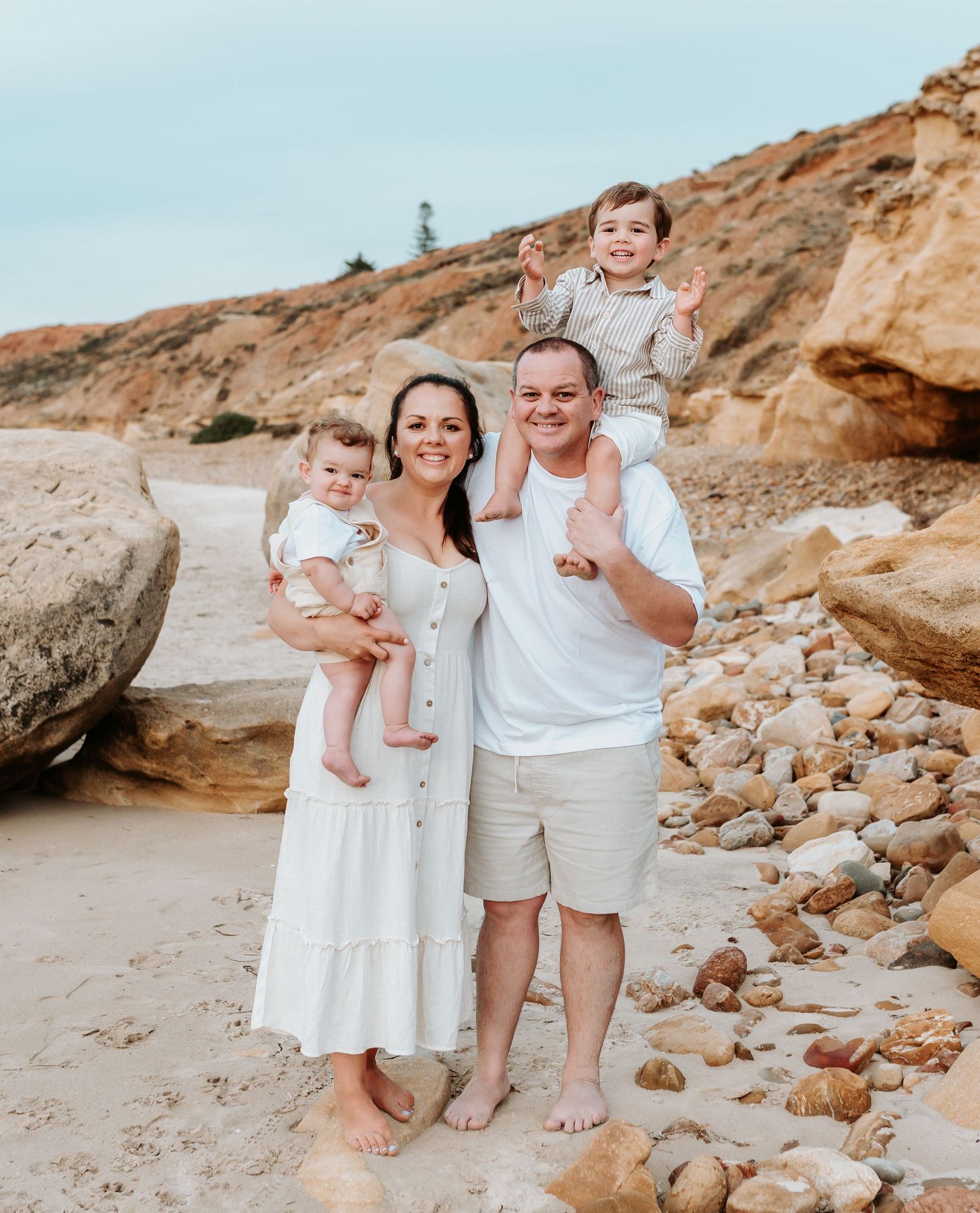 Family portrait session on a beach with everyone dressed in white against a backdrop of coastal cliffs.
