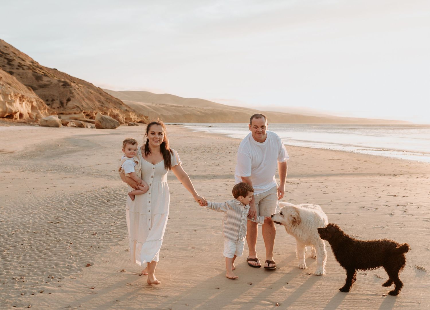Family walking along the beach at sunset with their dogs joining the fun.