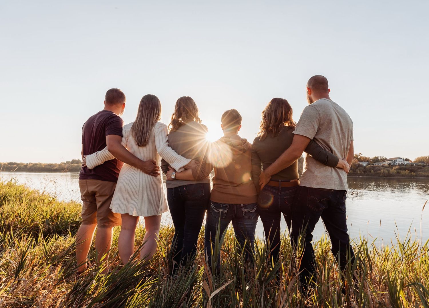 Group stands together watching sunset by a lake in warm golden light.