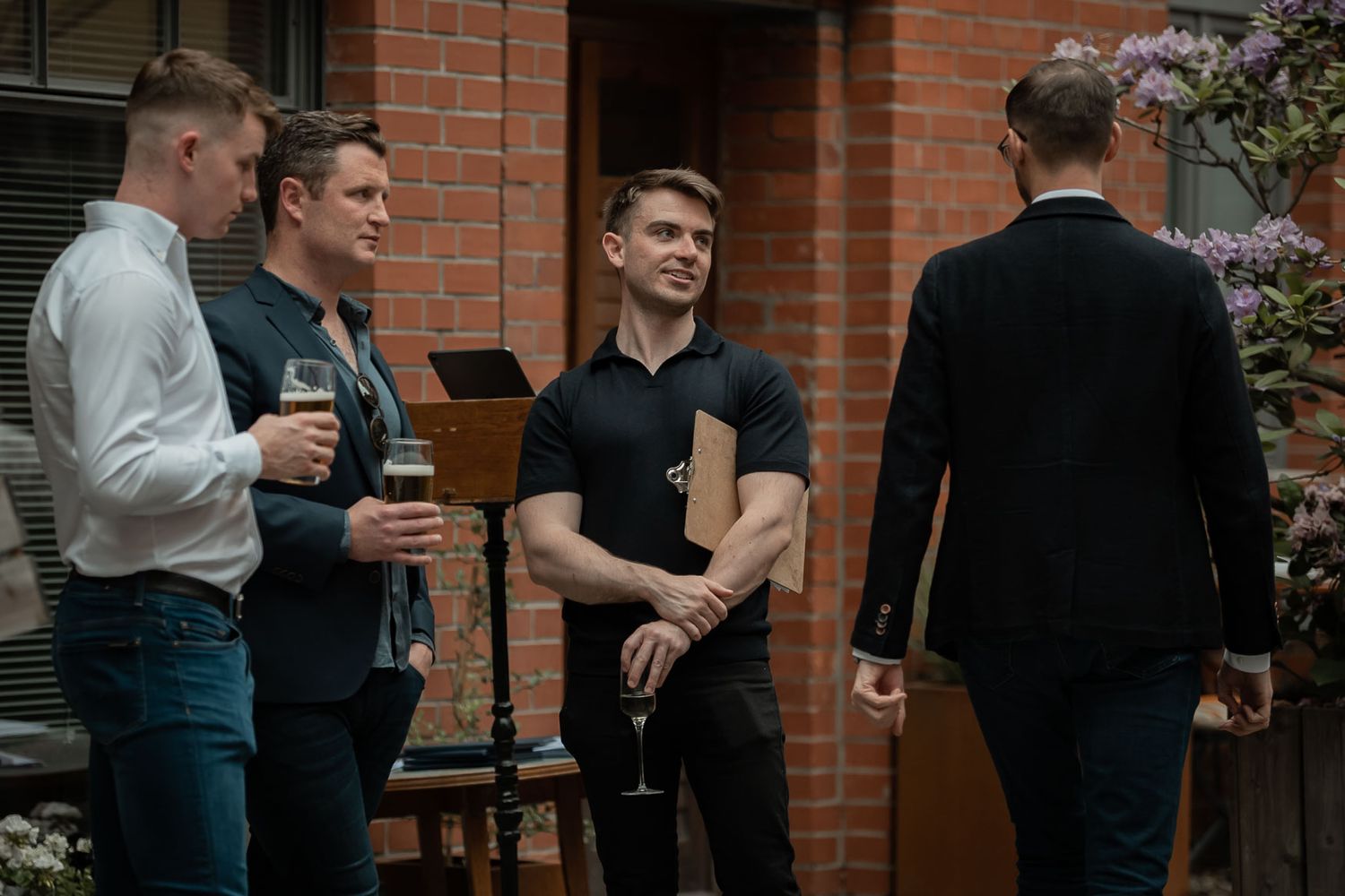 Group of young men having drinks and conversation outside brick building.