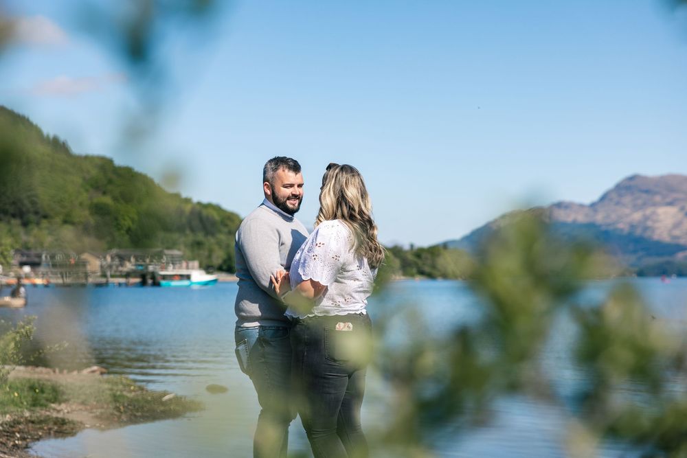 A couple shares a tender moment against a backdrop of a scenic mountain lake.