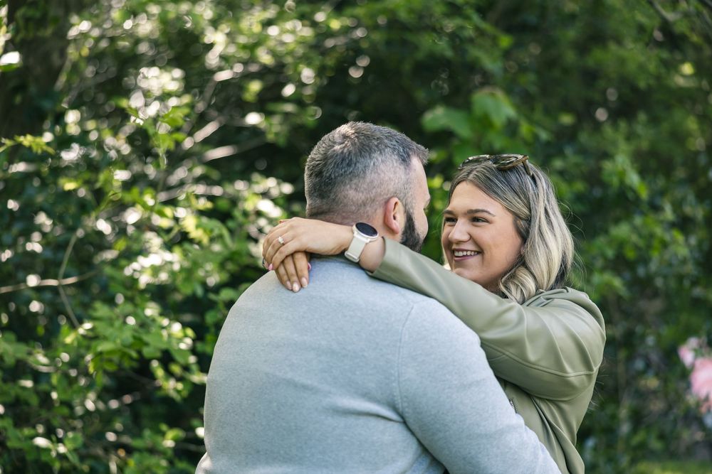A couple shares an intimate moment surrounded by blooming white flowers and greenery.