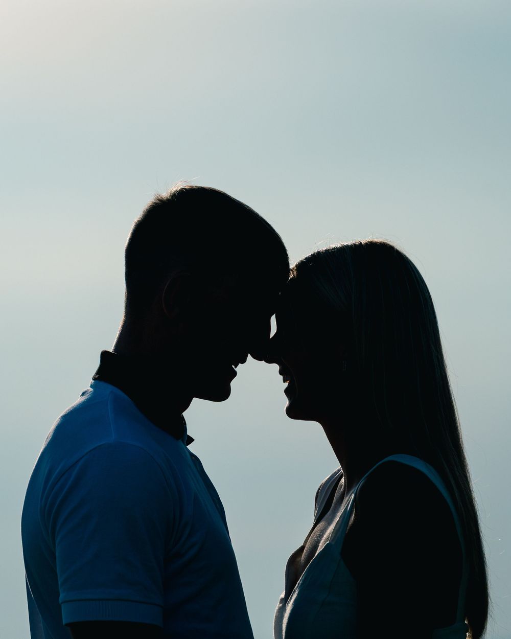 Silhouetted couple against blue sky background in romantic pose.