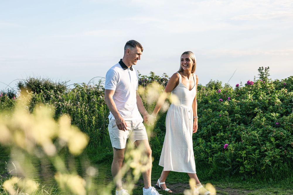 Couple walking through a sunny garden with white flowers and greenery in summer.