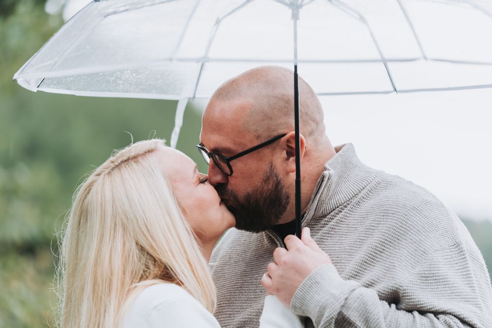 Couple sharing a romantic moment under white umbrellas in a garden setting.