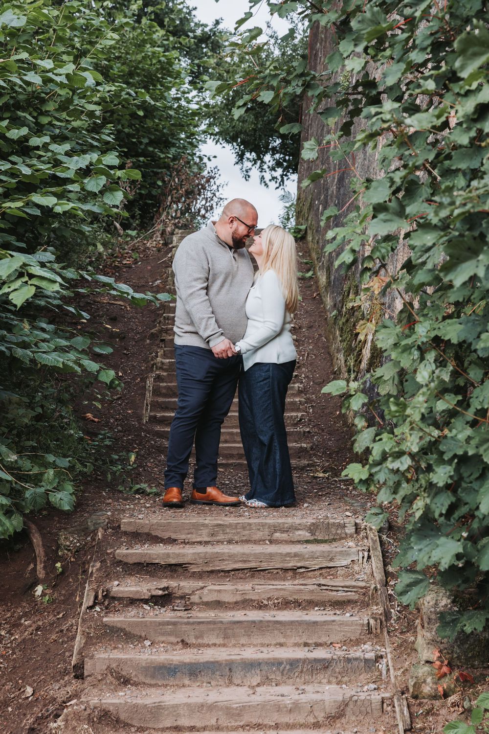 Couple sharing an intimate moment on rustic wooden steps surrounded by green foliage.