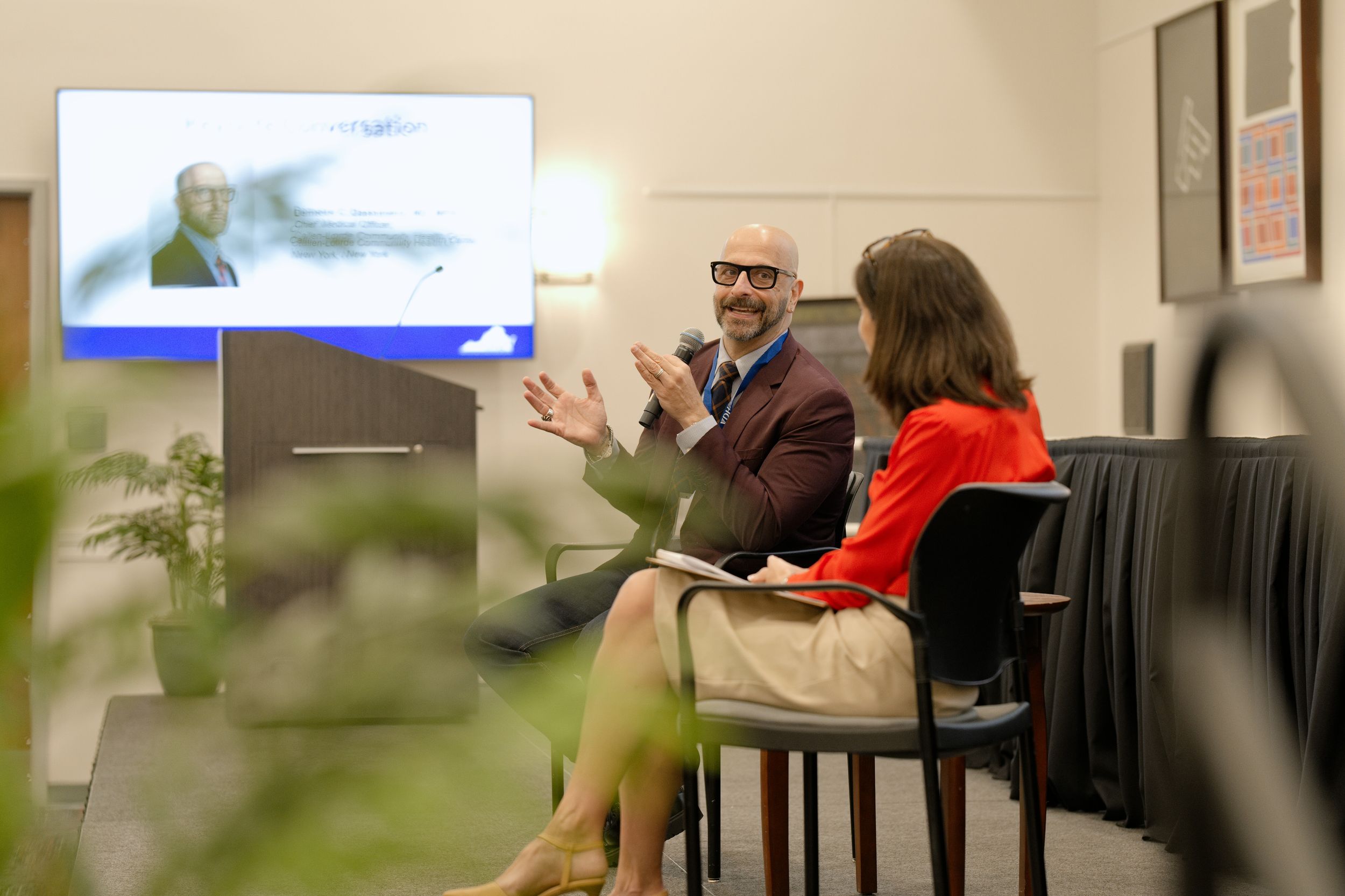 Two professionals engage in conversation in a modern office setting with a video conference screen in the background. RVA Event photography