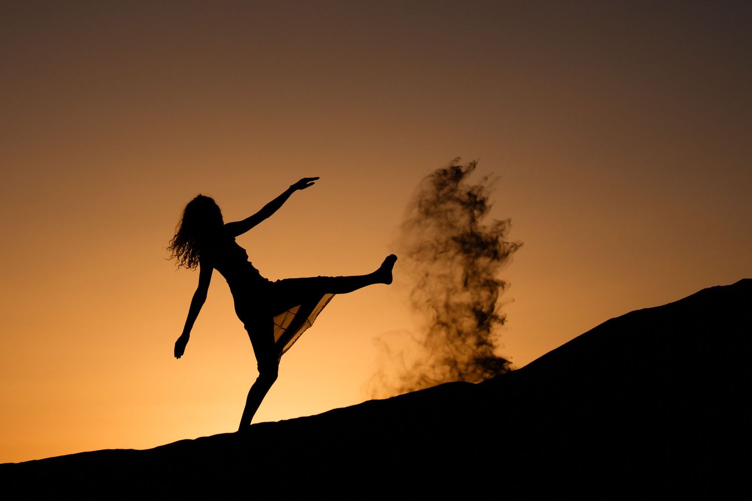 Silhouette of a woman dancing gracefully at sunset with a golden sky and misty background.
