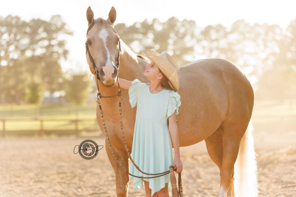 Young girl in mint dress and cowboy hat affectionately nuzzling palomino horse at sunset.