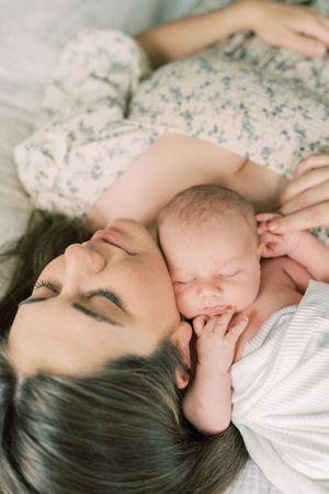A tender moment between a parent and newborn baby lying together on white bedding with a floral print dress.