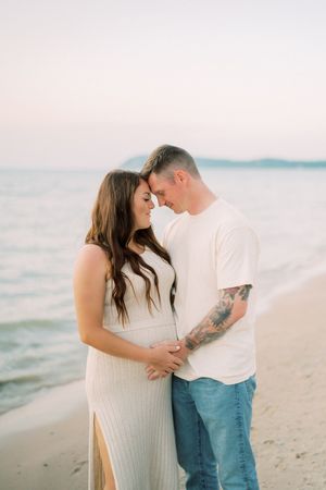 Romantic couple shares intimate moments along a tranquil beach at sunset with dreamy pastel colors in the background.