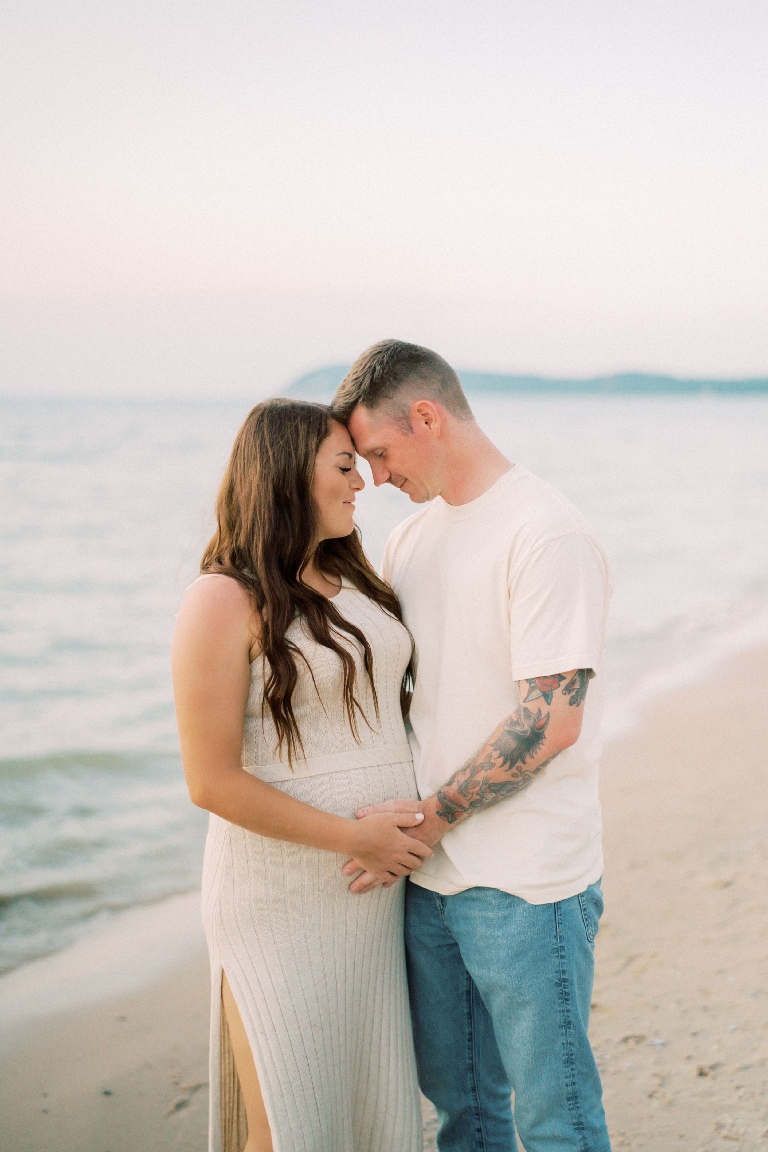 Romantic couple shares intimate moments along a tranquil beach at sunset with dreamy pastel colors in the background.