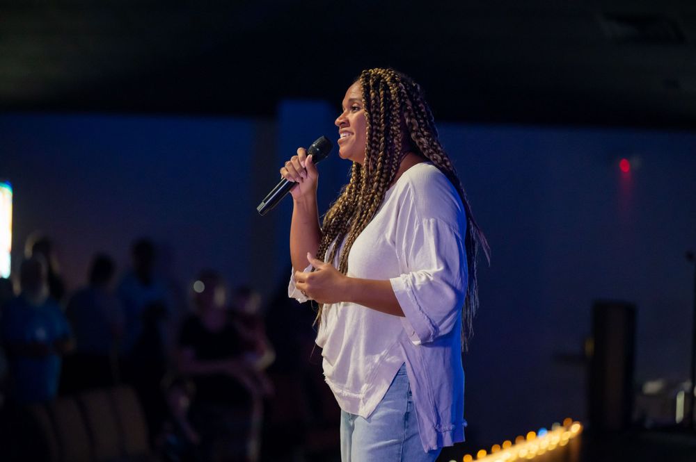 A performer in a white shirt singing passionately on stage with dramatic blue lighting.