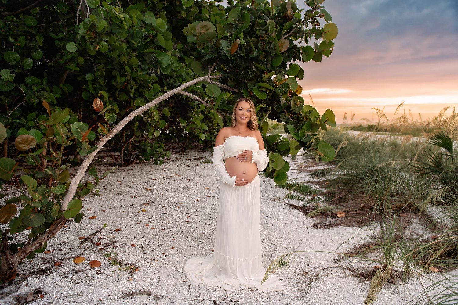 A peaceful beach scene with white sand and tropical foliage at sunset.