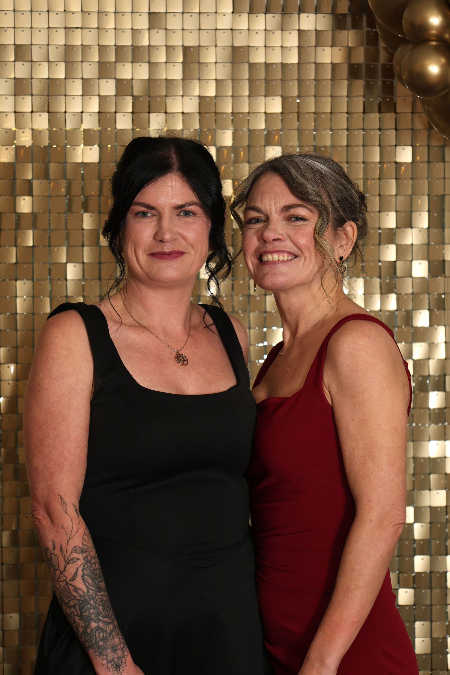 Two people posing together in front of a sparkly gold sequin backdrop at an event.