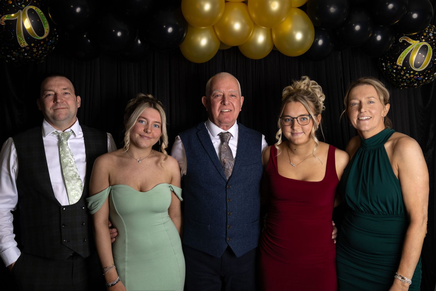 A group of formally dressed people pose together for an elegant event photo against a dark background.