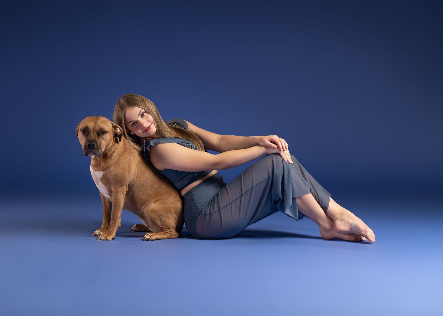 A dancer posing with a dog on a blue backdrop.