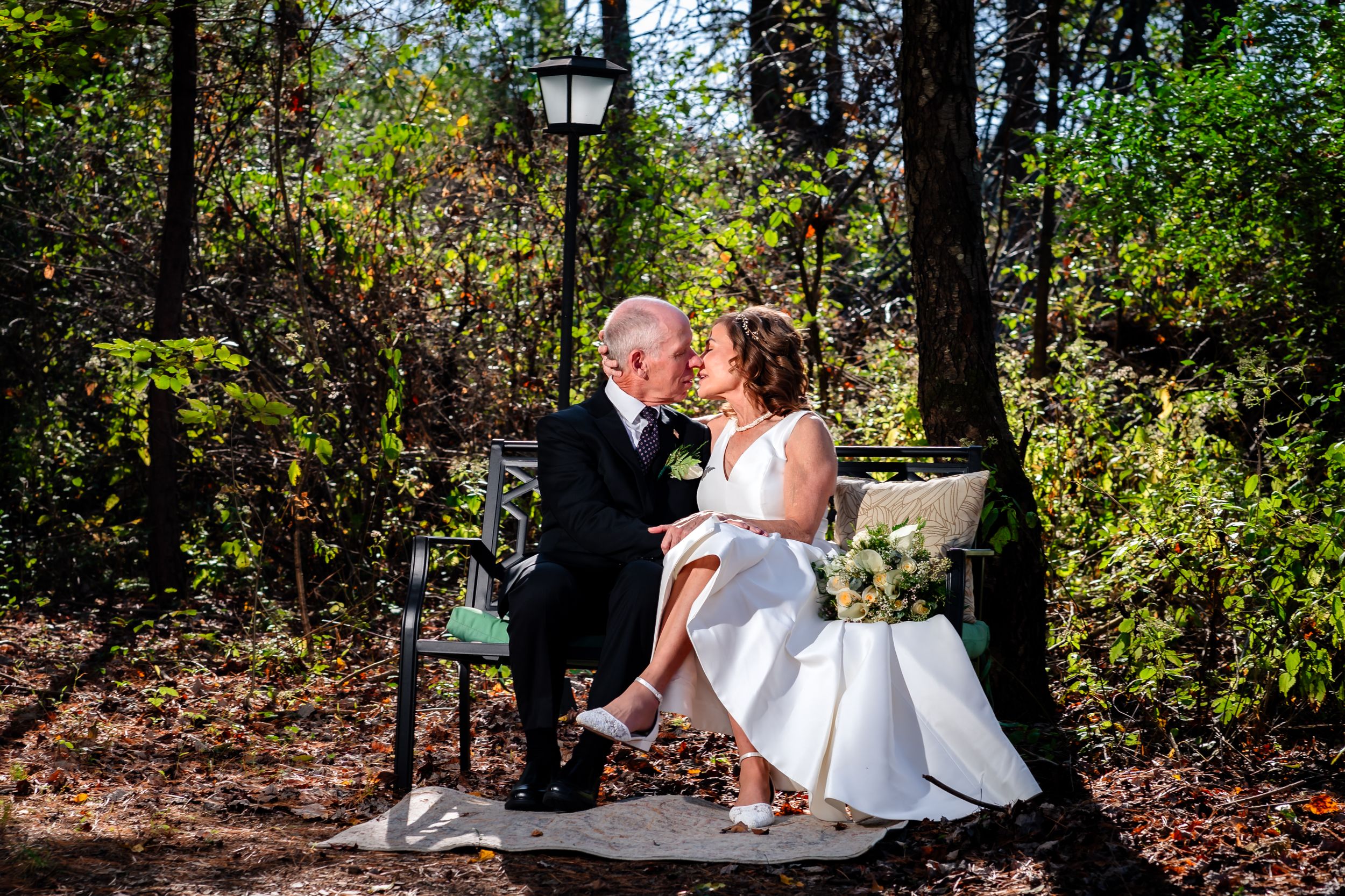 Wedding couple shares intimate moments among trees and autumn foliage in a wooded setting.
