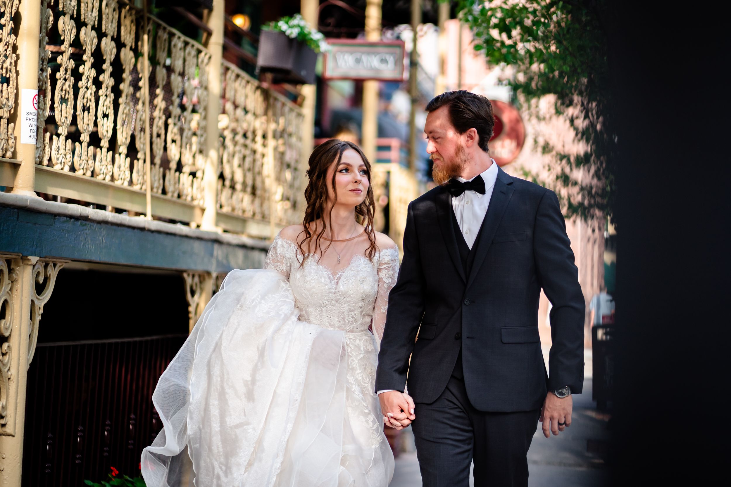 Elegant wedding couple walking and embracing along a decorative railing during golden hour.